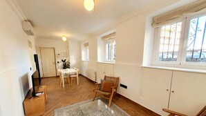 A spacious living room with a large window, a dining area with a table and chairs, and a cozy seating area with a patterned rug. - Collection Madrid R o Est Ndar 4 Personas (Madrid)