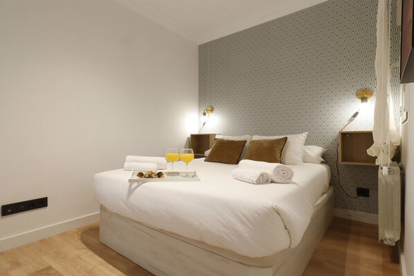 A neatly made bed with white linens, two bedside lamps, a tray with a bottle and glasses, and a patterned wall. - Collection Madrid R o Est Ndar 4 Personas (Madrid)