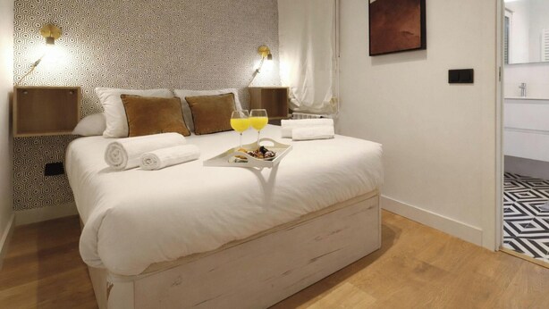 A hotel room with a bed, bedside tables, a nightstand, a bedside lamp, a tray with snacks, and a bathroom with a sink and mirror. - Collection Madrid R o Est Ndar 4 Personas (Madrid)