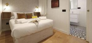 A hotel room with a bed, bedside tables, a nightstand, a bedside lamp, a tray with snacks, and a bathroom with a sink and mirror. - Collection Madrid R o Est Ndar 4 Personas (Madrid)
