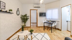 A modern living room with a dining area, featuring a wooden floor, a round white table, and a black TV on the wall. - C Plaza de Espa a 4B (Madrid)