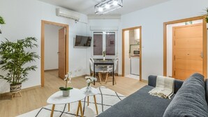 A modern living room with a grey sofa, a small dining table, and a kitchen area with a TV. - C Plaza de Espa a 4B (Madrid)