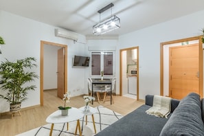 A modern living room with a grey sofa, a small dining table, and a kitchen area with a TV. - C Plaza de Espa a 4B (Madrid)