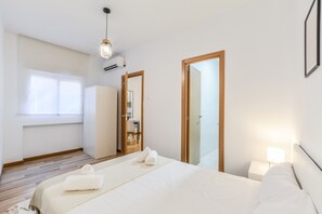 Une chambre d’hôtel moderne dotée d’un grand lit, d’une table de chevet avec une lampe, d’une armoire et d’une fenêtre avec des stores.