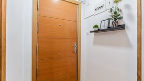A wooden door with a handle and a sign above it. There is a shelf with decorative items and a small plant on the wall. - C Plaza de Espa a 4B (Madrid)