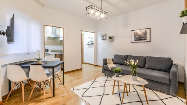 A modern living room with a grey sofa, a dining table with chairs, a kitchen in the background, and a large mirror on the wall. - C Plaza de Espa a 4B (Madrid)
