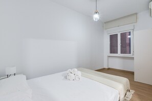 Ένα μινιμαλιστικό υπνοδωμάτιο με ένα μονό κρεβάτι, ένα κομοδίνο με ένα φωτιστικό, ένα παράθυρο με περσίδες και ένα φωτιστικό οροφής.