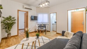 A modern living room with a grey sofa, a small dining table with chairs, a TV mounted on the wall, and a wooden door. - C Plaza de Espa a 4B (Madrid)