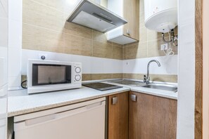 Μια σύγχρονη κουζίνα με φούρνο μικροκυμάτων, κουζίνα, νεροχύτη και ξύλινα ντουλάπια.