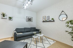 Ein modernes Wohnzimmer mit einem grauen Sofa, zwei weißen runden Tischen, einem schwarz-weißen Teppich und einer Deckenleuchte.