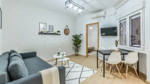 A modern living room with a grey sofa, a dining table with chairs, a TV mounted on the wall, and a potted plant. - C Plaza de Espa a 4B (Madrid)