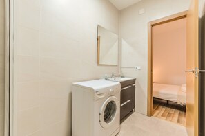 Una habitación de hotel compacta con lavadora, un lavabo y una cama.