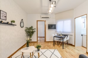 A modern living room with a dining area, featuring a wooden floor, a round white table, and a black TV on the wall. - C Plaza de Espa a 4B (Madrid)