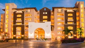 A multi-story hotel with a central archway entrance, balconies on each floor, and a paved courtyard.
