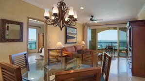 A spacious dining area with a glass table and wooden chairs, a chandelier, and a view of the ocean through large sliding doors.
