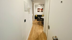 A hallway leading to a living area with a sofa, a table, and a coffee table. There is a phone on the wall and a door with a handle. - C Madrid R o 2 F in Madrid (Madrid)