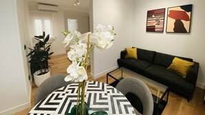 A modern living room with a black sofa, a dining table with a geometric tablecloth, and a vase of white orchids. There are two paintings on the wall and an air conditioning unit in the background. - C Madrid R o 2 F in Madrid (Madrid)