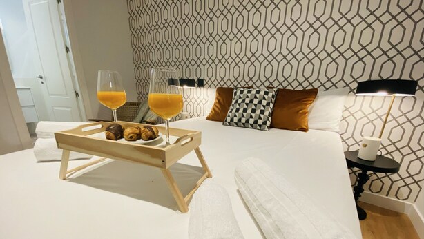 A neatly made bed with white linens, a tray with croissants and orange juice, and a patterned wall in the background. - C Madrid R o 2 F in Madrid (Madrid)
