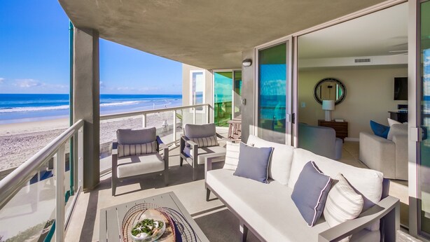 Ein Balkon mit Blick auf den Strand, ausgestattet mit einer Couch und Sesseln sowie einem Essbereich mit Tisch und Stühlen.
