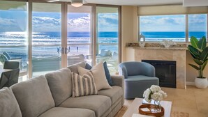Ein Wohnzimmer mit großem Fenster zum Strand, Deckenventilator und Kamin.