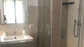 A modern bathroom with a glass-enclosed shower, a sink with a mirror above, and a patterned rug on the floor. - R home room 19 (Ischia)