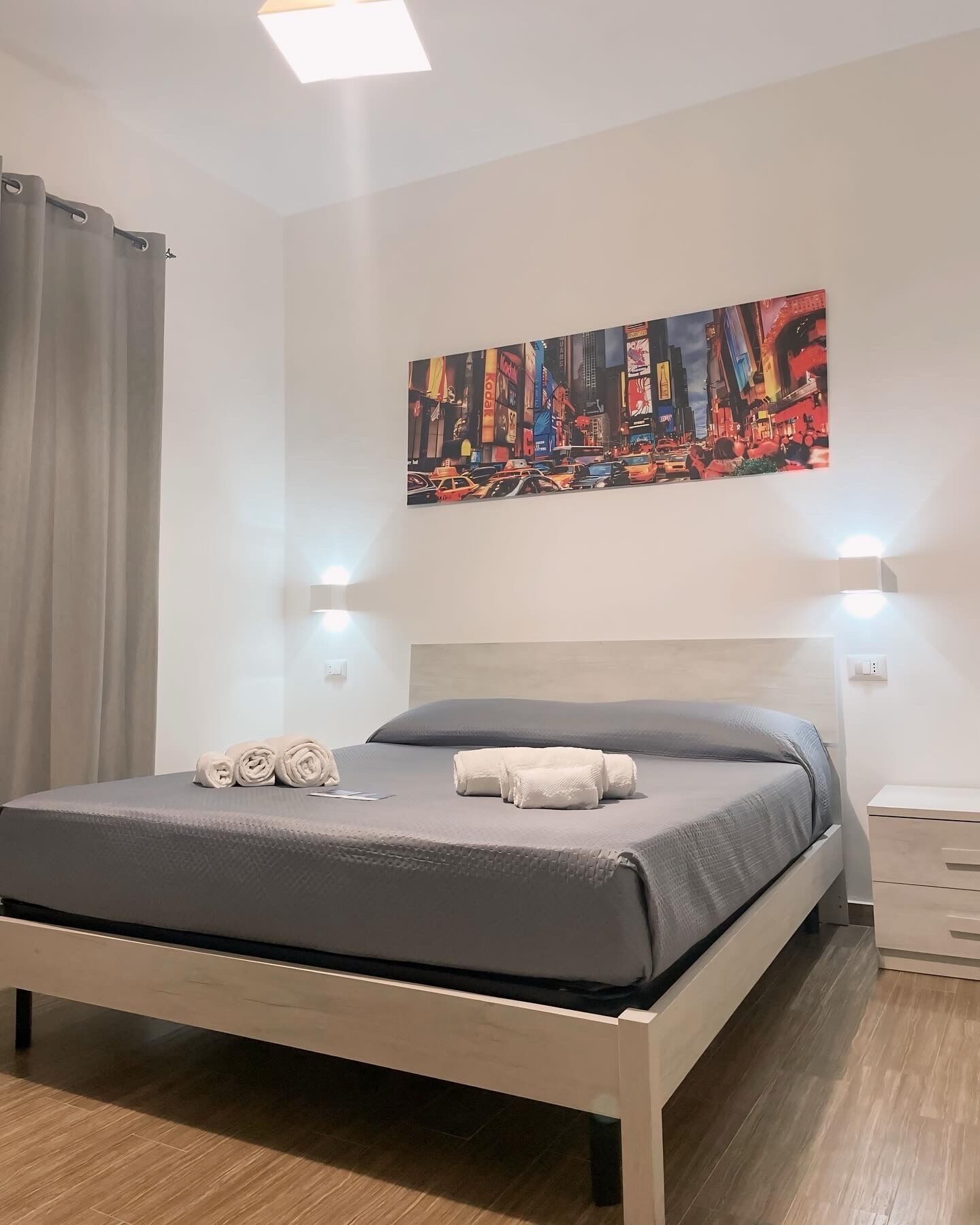Een moderne slaapkamer met een bed, een stadsgezicht op canvas en twee wandlampen.