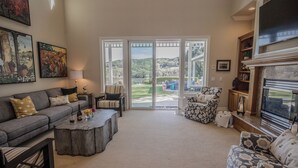 Un salon avec un canapé gris, un fauteuil à motifs, une table basse et une cheminée. De grandes portes vitrées donnent sur un patio aménagé avec du mobilier d’extérieur.
