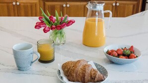 Un plateau de petit-déjeuner comprenant un croissant, du jus d’orange, des fraises et des tulipes, disposés sur un comptoir en marbre.