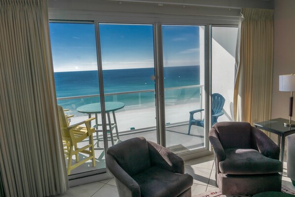 A balcony with a view of the ocean, a table, two chairs, and a lamp.