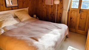 Et soveværelse med træpaneler, en seng, et natbord, en lampe og et vindue med gardiner.