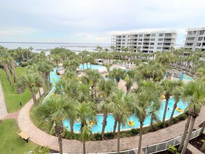 Een resort met een zwembad in het midden, omgeven door palmbomen, ligbedden en uitzicht op de oceaan.