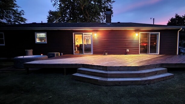 Een huis met een houten terras, een schuifpui en een schoorsteen.