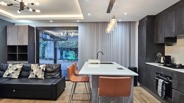 A modern kitchen with a central island, bar stools, a built-in oven, and a dining area with a sofa and chairs.