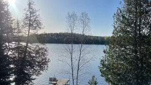 A lakeside view with a dock and chairs, surrounded by trees and a grassy area. - Caribou Sunrise, Lakeside Cabin in the Northwoods! (Lutsen)