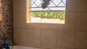 A rectangular bathtub with a window above it, a towel rack, and a toilet brush.