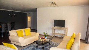 A living room with a sofa set, a coffee table, a TV on a stand, and a chandelier.