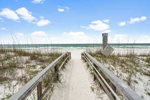 Ein Sandweg am Strand, der zum Meer führt, mit einem hölzernen Steg und einem Wegweiser.