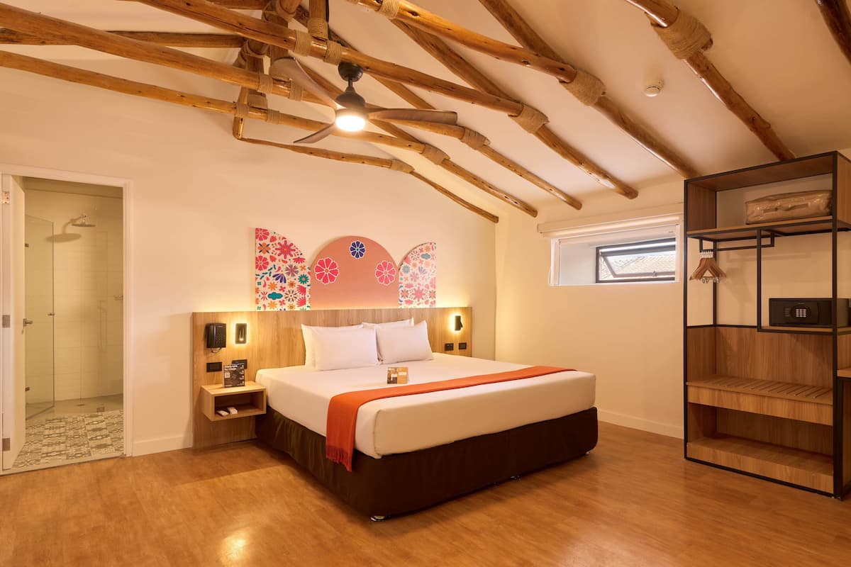 Ein Schlafzimmer mit einem großen Bett, Holzbalkendecke, einem Nachttisch, einem an der Wand montierten Fernseher und einem Fenster mit Blick.