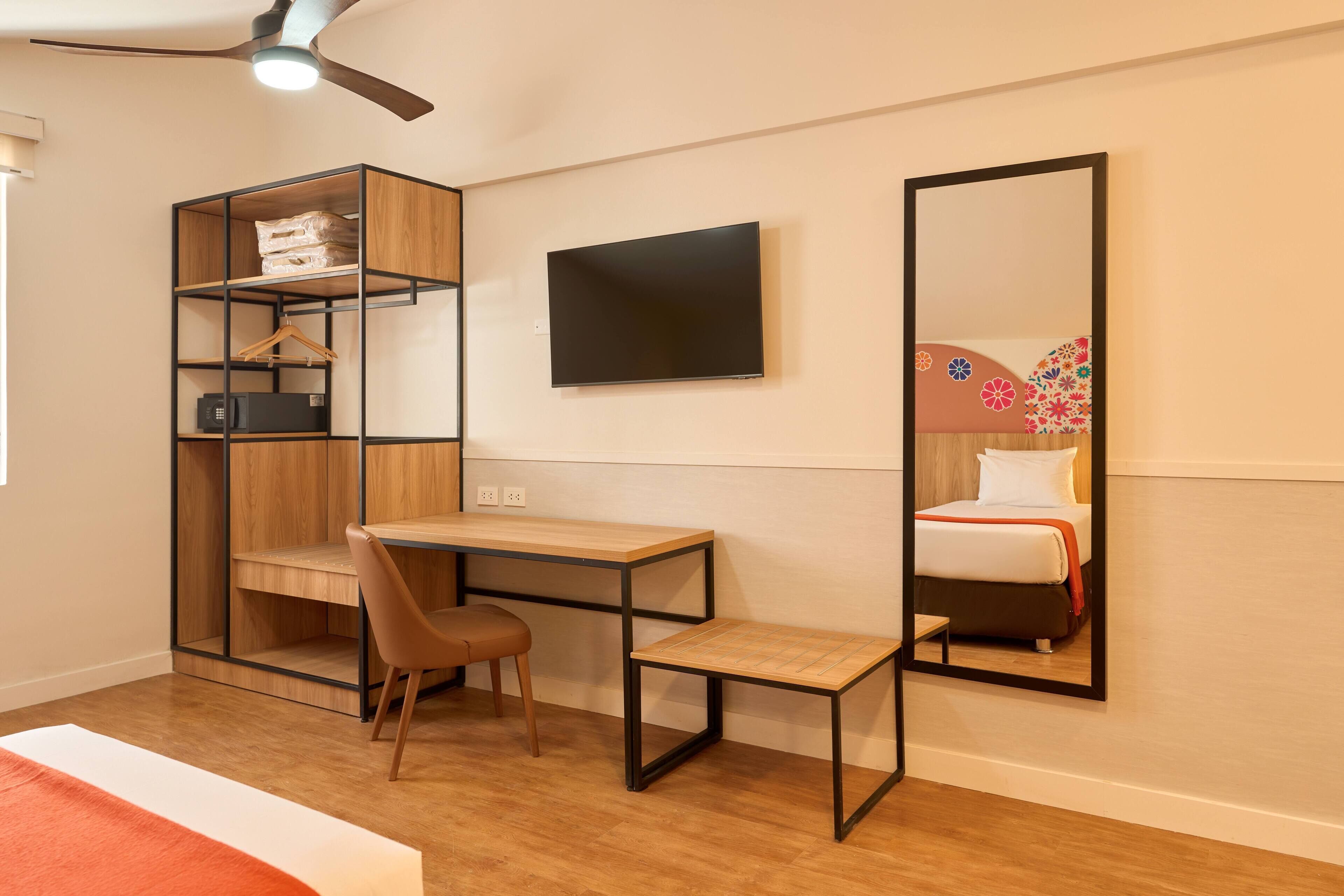 A bedroom with a bed, a desk, a chair, a wardrobe, a TV, and a mirror.