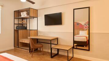 A bedroom with a bed, a desk, a chair, a wardrobe, a TV, and a mirror.
