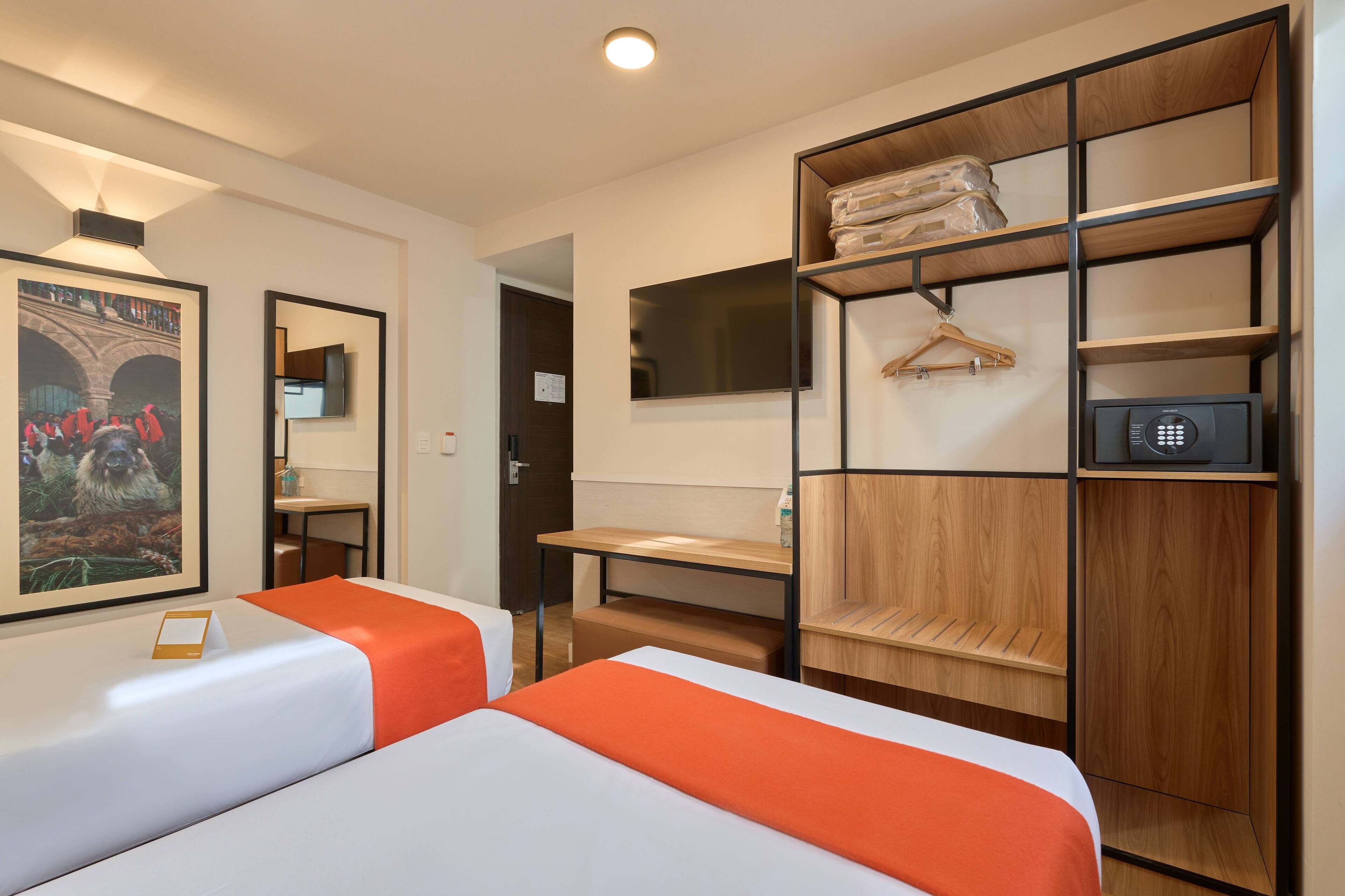 A hotel room with two beds, a wooden wardrobe, a desk, and a mirror.