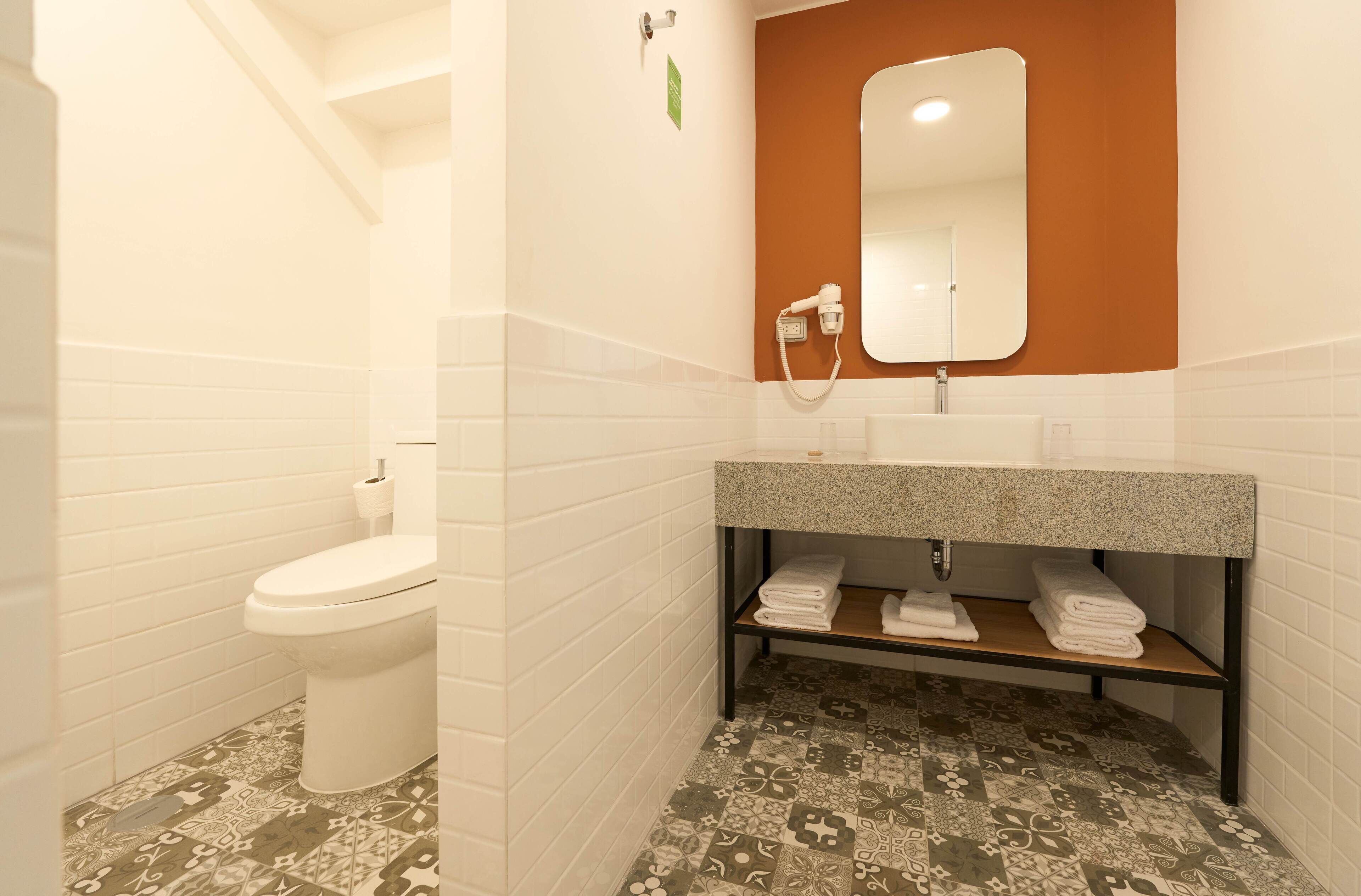 A bathroom with a white toilet, a sink with a mirror above it, and a shelf with folded towels.