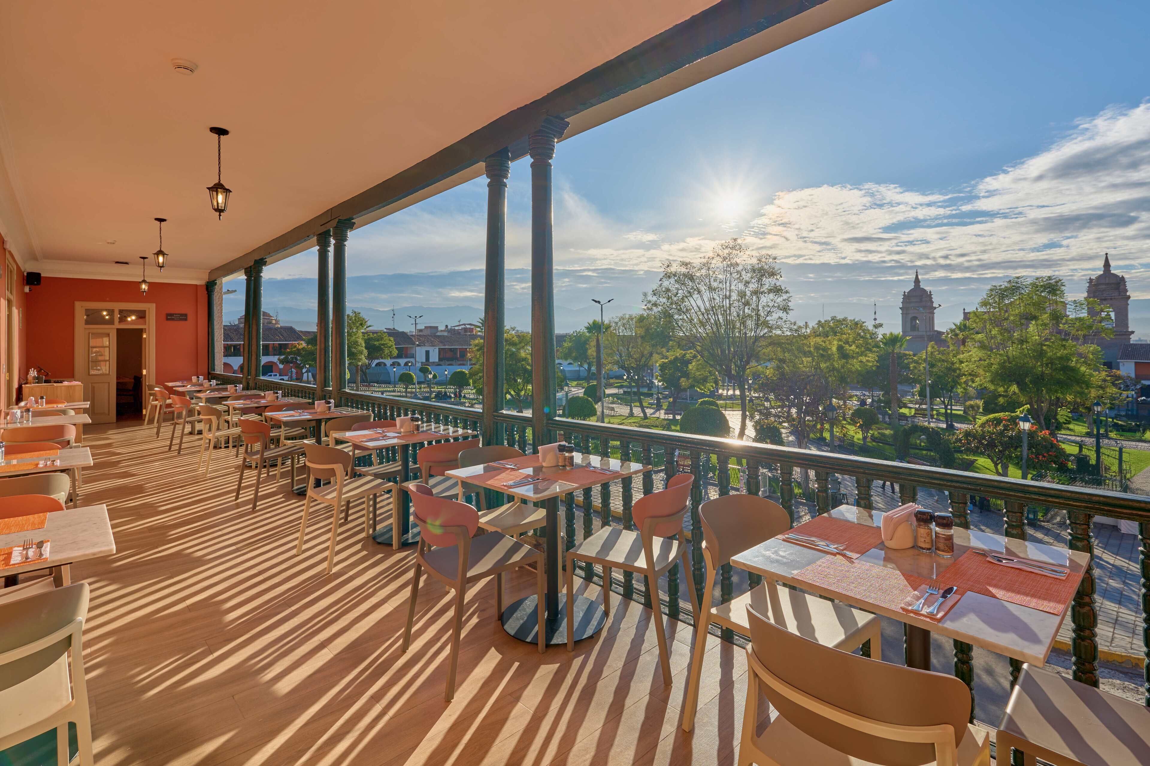 A restaurant with outdoor seating, large windows, and a view of a cityscape.