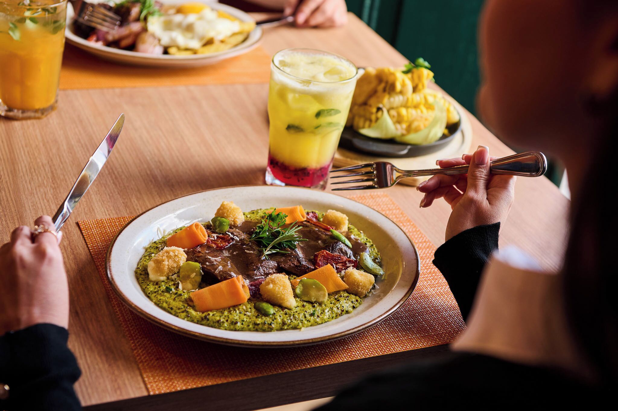 A dining table with a plate of food, a glass of drink, and a fork.