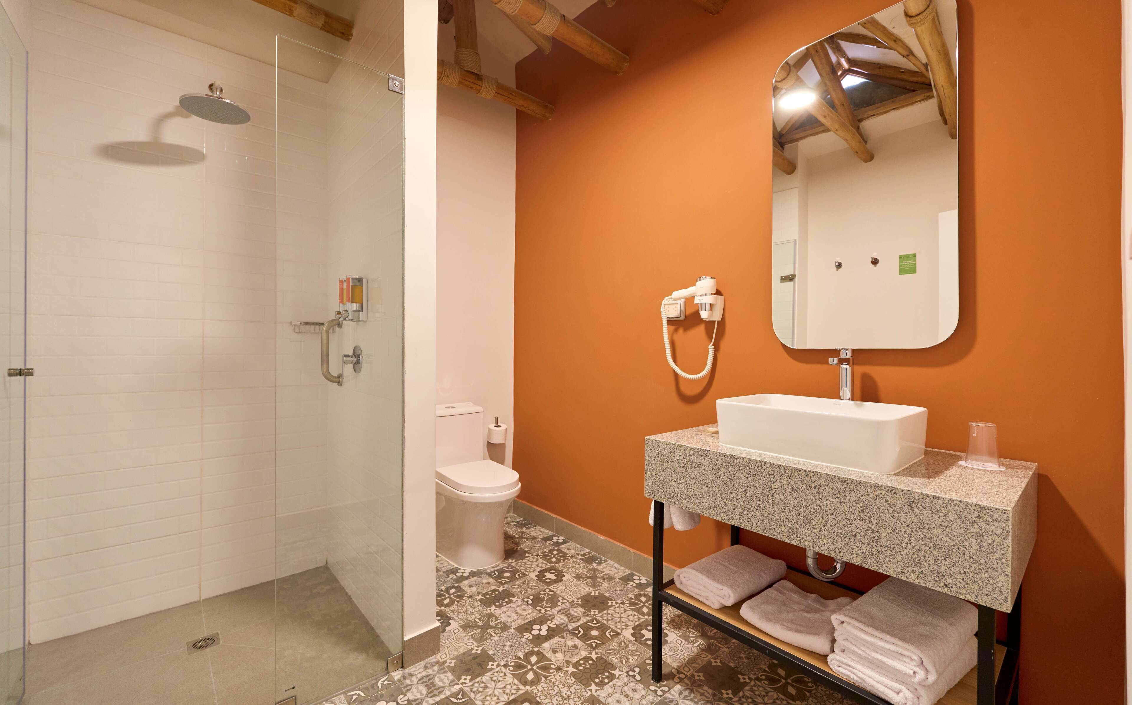 Un baño con cabina de ducha de vidrio, inodoro y lavamanos con toallero.