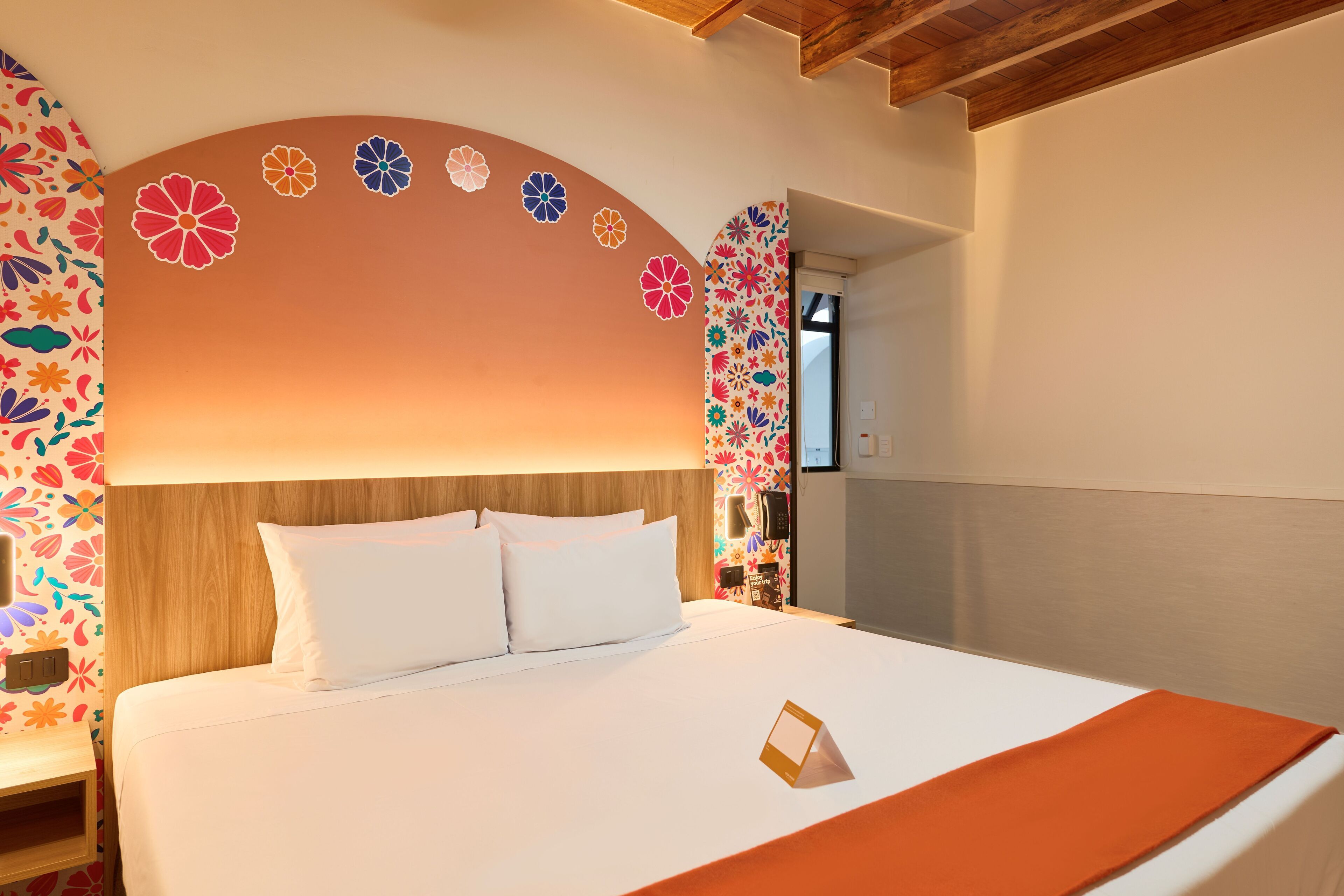 Een hotelkamer met een groot bed, een houten hoofdbord en kleurrijke bloemenkunst aan de muur.