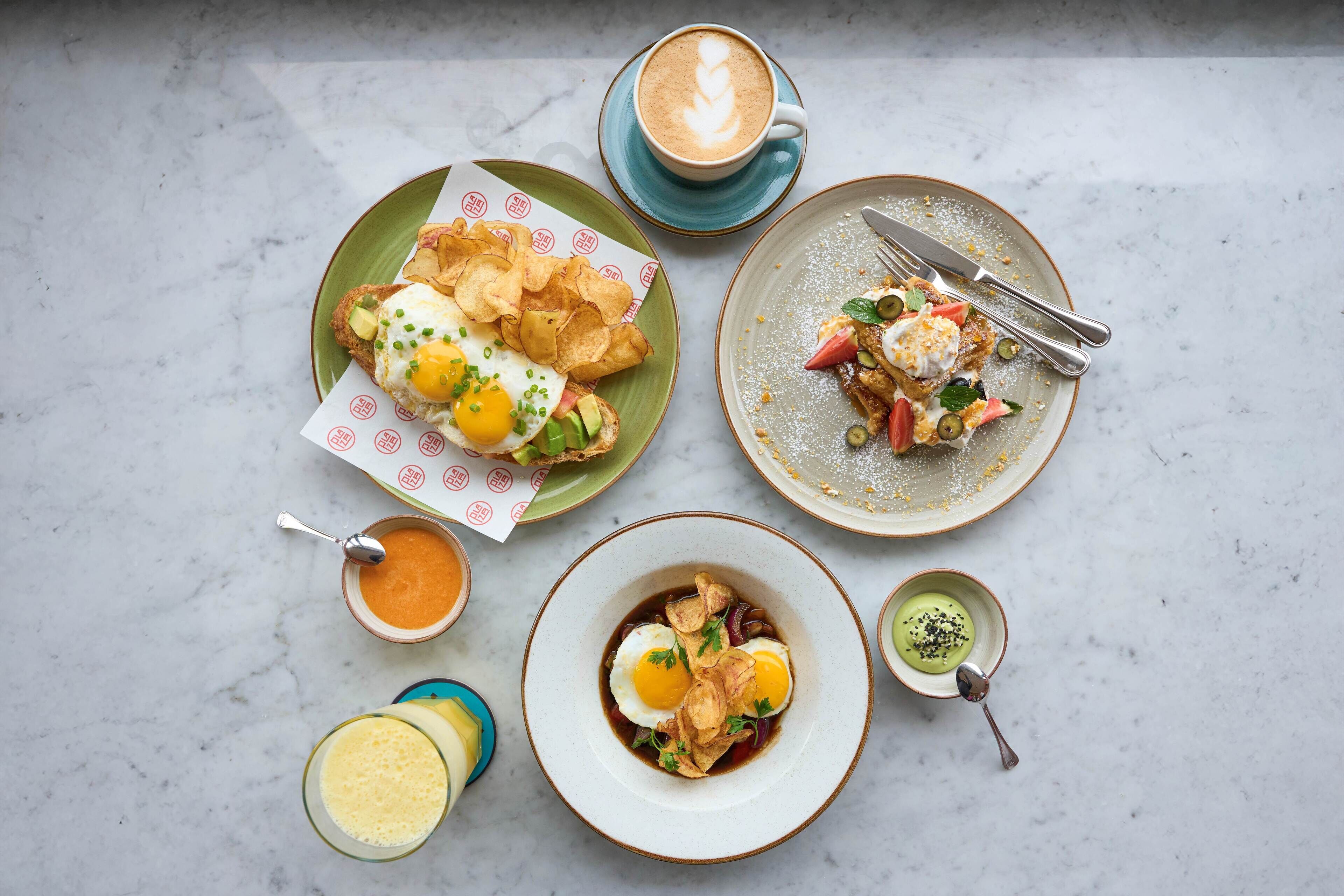 Variedad de platos que incluyen huevos fritos, una taza de café y varios recipientes pequeños con salsas y aderezos.