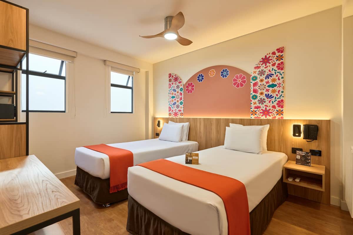 Ein Hotelzimmer mit zwei Betten, einem Schreibtisch und einem Deckenventilator.