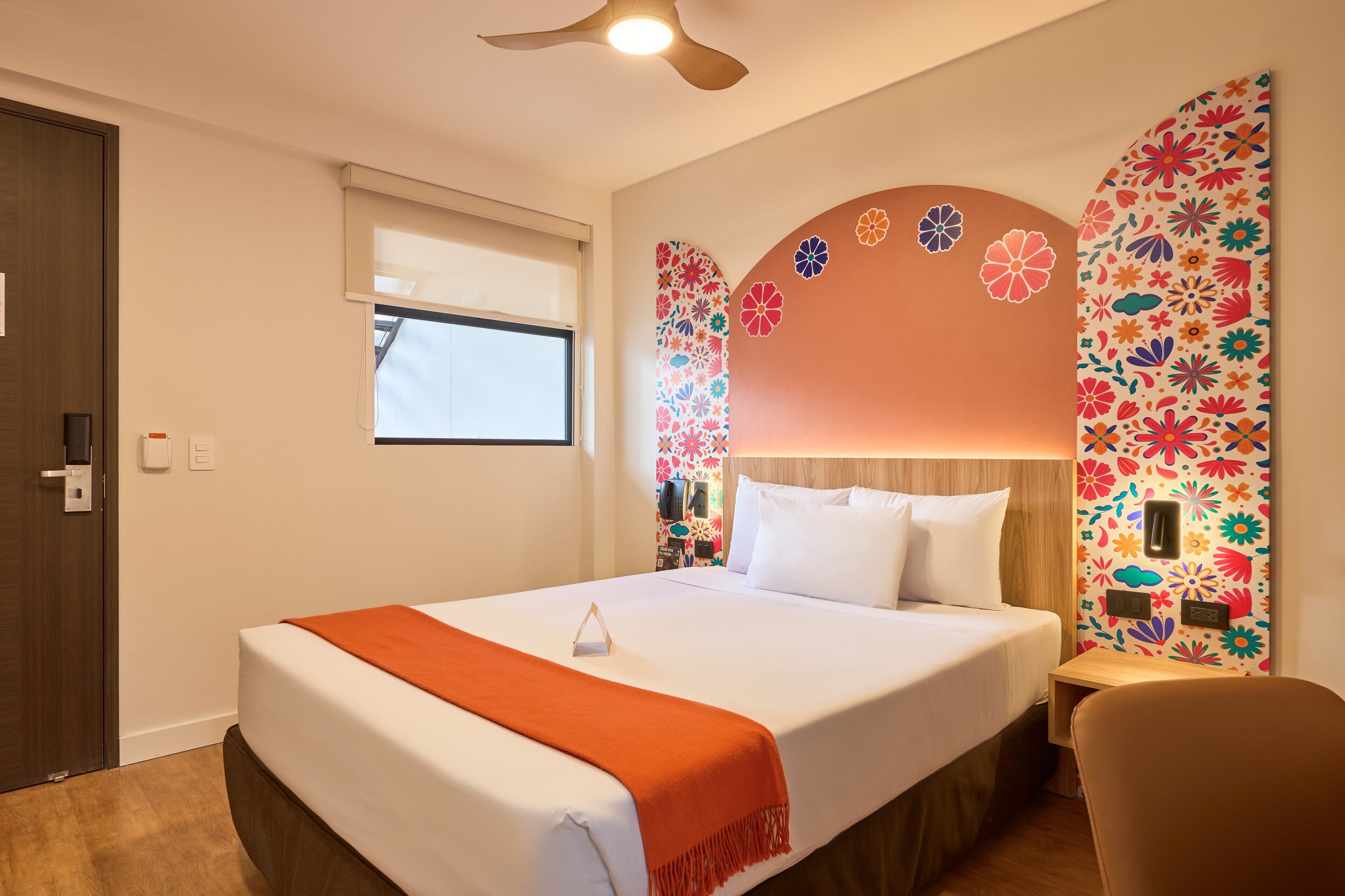 Habitación de hotel con cama, ventana, ventilador de techo y pared con estampado floral.