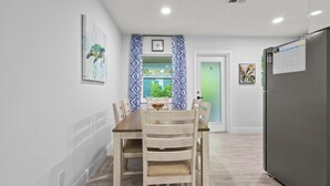 Un coin repas avec une table et des chaises en bois, une horloge au mur et une fenêtre agrémentée de rideaux à motifs.